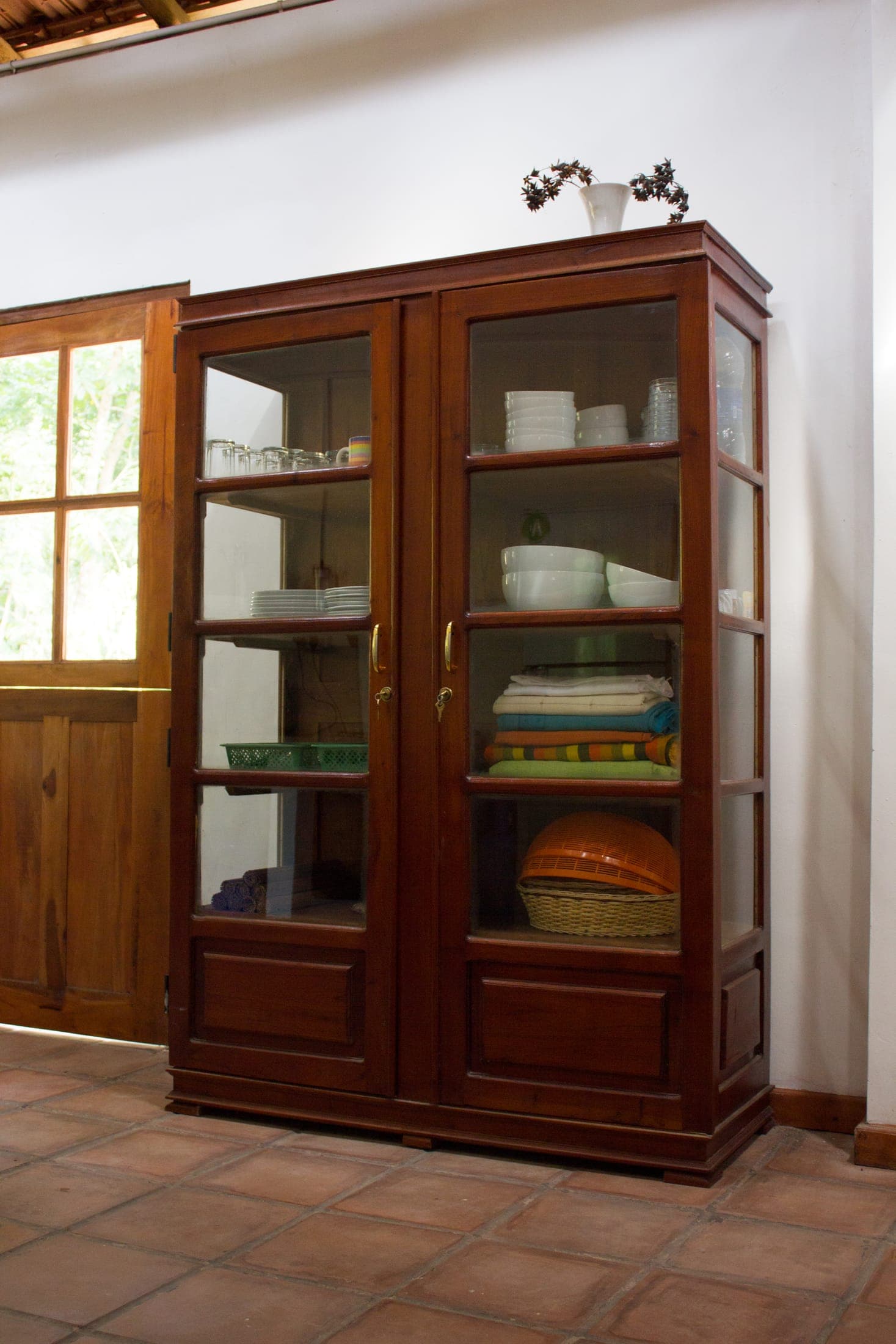 Glass-fronted teak cupboard stocked with linen and crockery