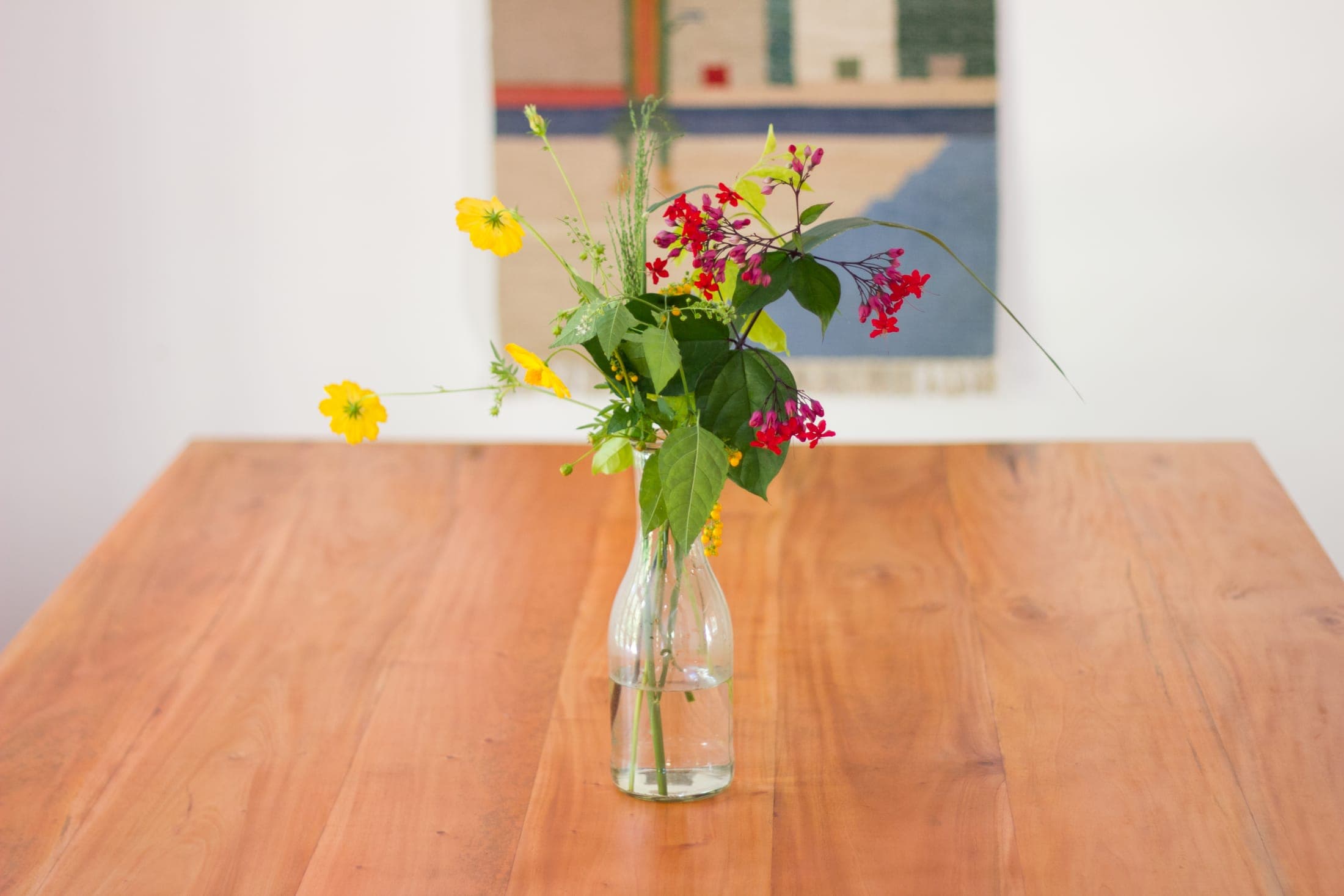 Fresh garden flowers in a glass bottle on the wooden dining table