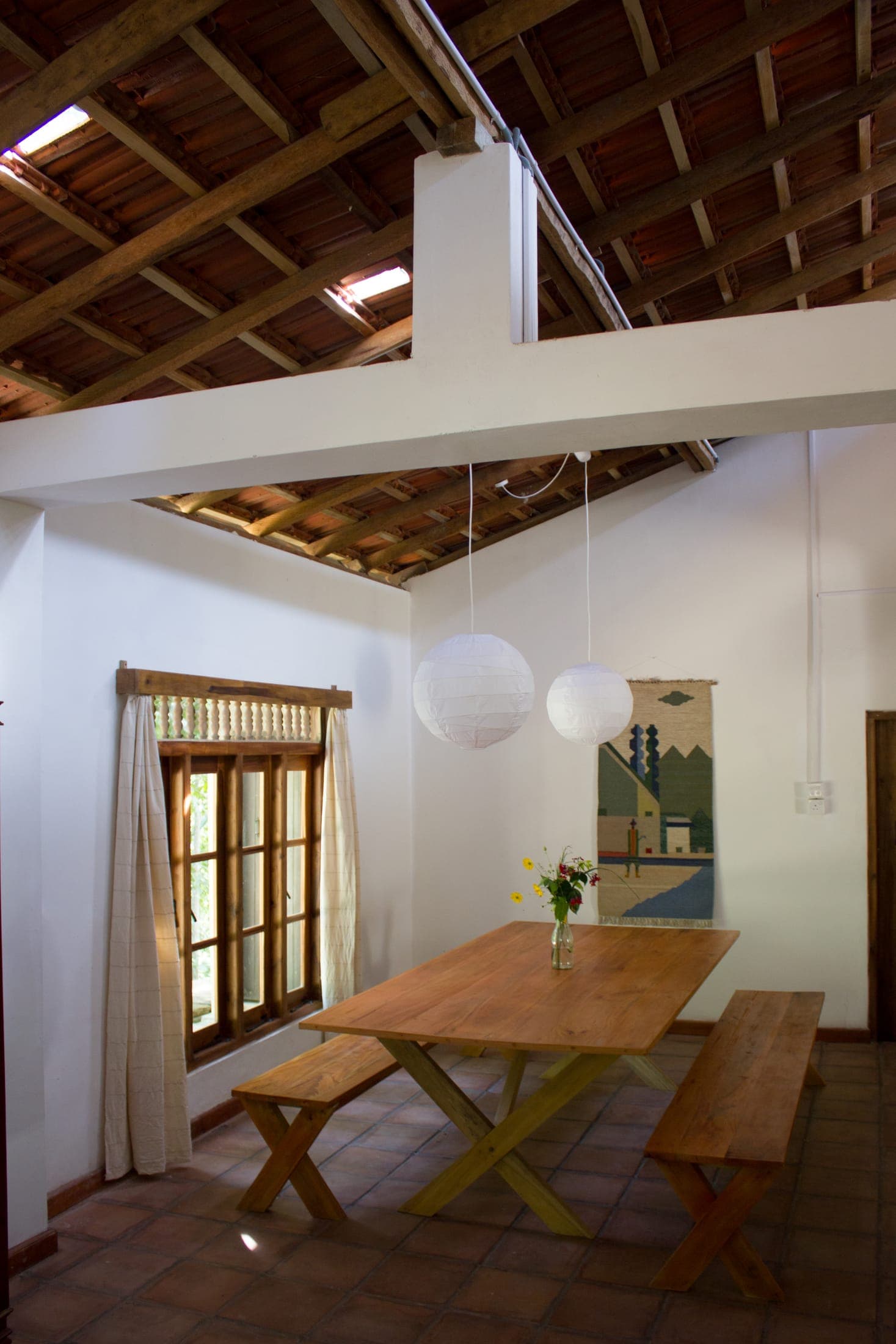 Dining area with paper lanterns, a woven wall hanging and a long wooden table