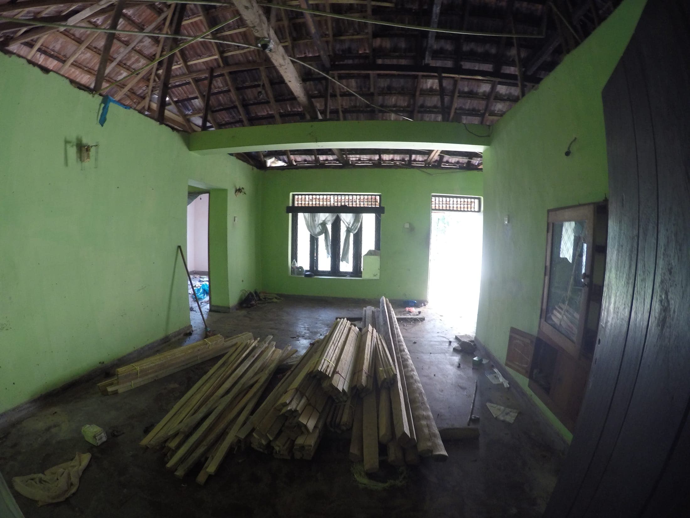 Inside the house before renovation: bare green walls and timber stacked for the new roof