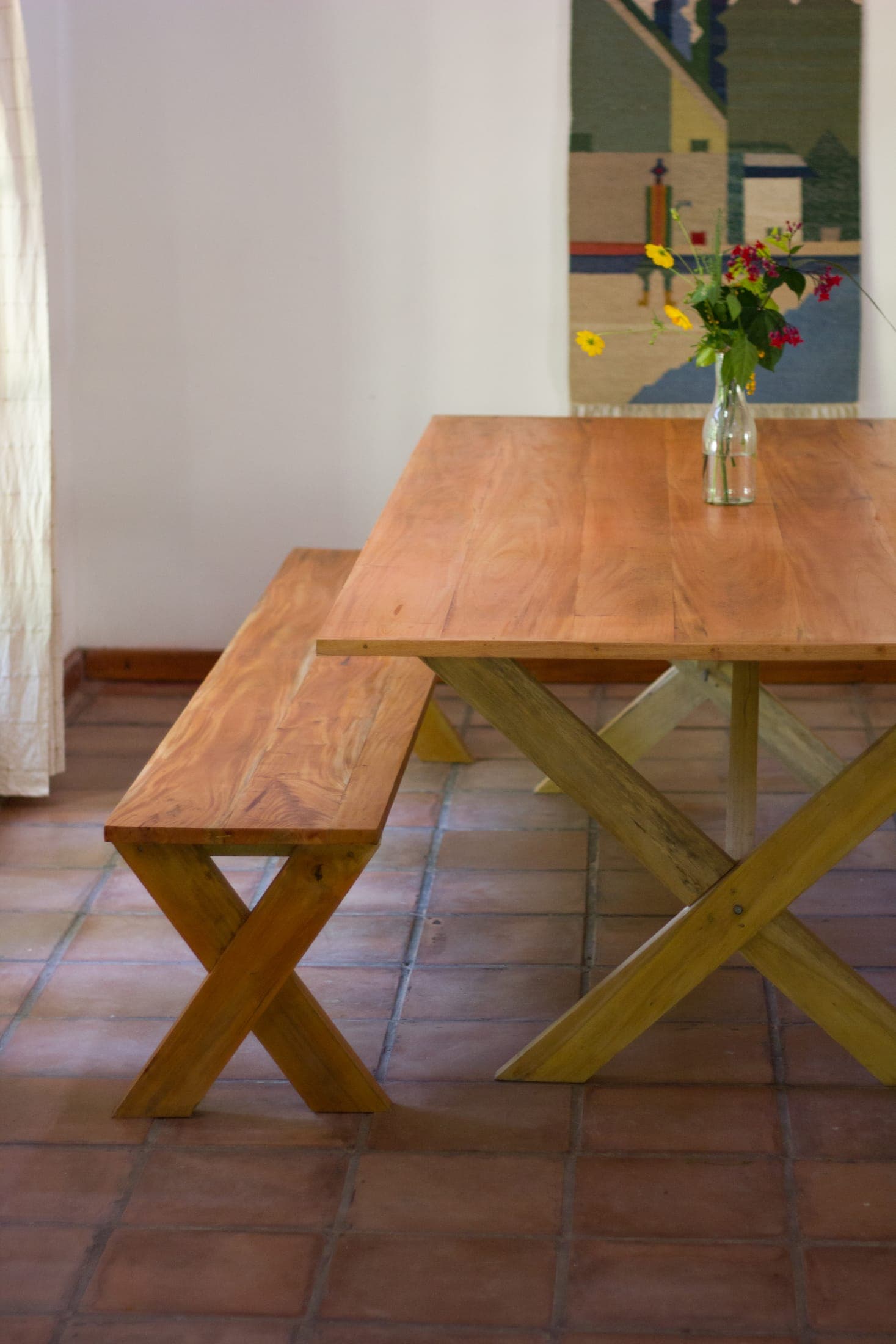 Handmade wooden dining table and bench on a terracotta tiled floor