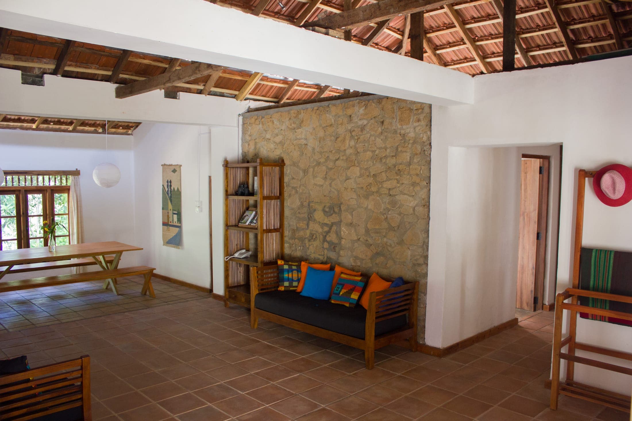 Open living room with a natural stone wall, terracotta floor tiles and an exposed timber roof
