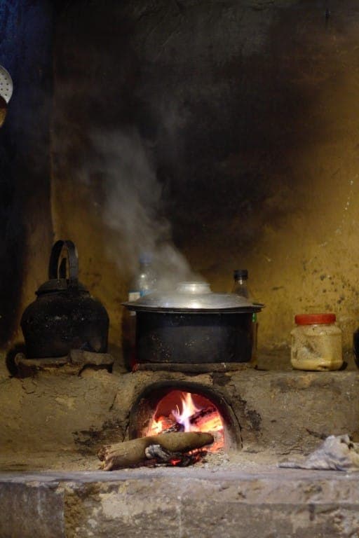 A traditional wood-fired hearth with a steaming pot in a village kitchen
